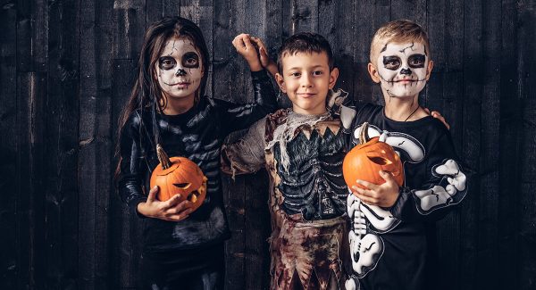 Three multiracial kids scary costumes posing with pumpkins old house halloween concept